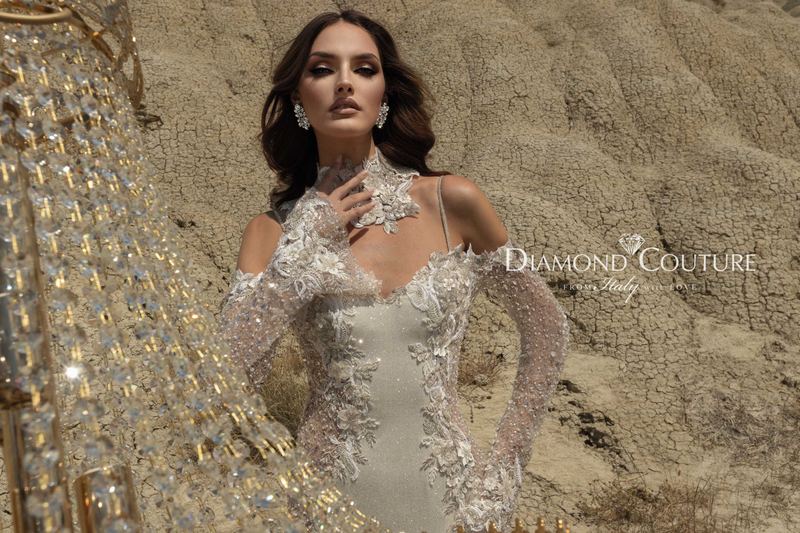 Abito da sposa Diamond Couture 2027: corpetto a cuore con pizzo in rilievo, maniche trasparenti e collarino in pizzo, tra i calanchi