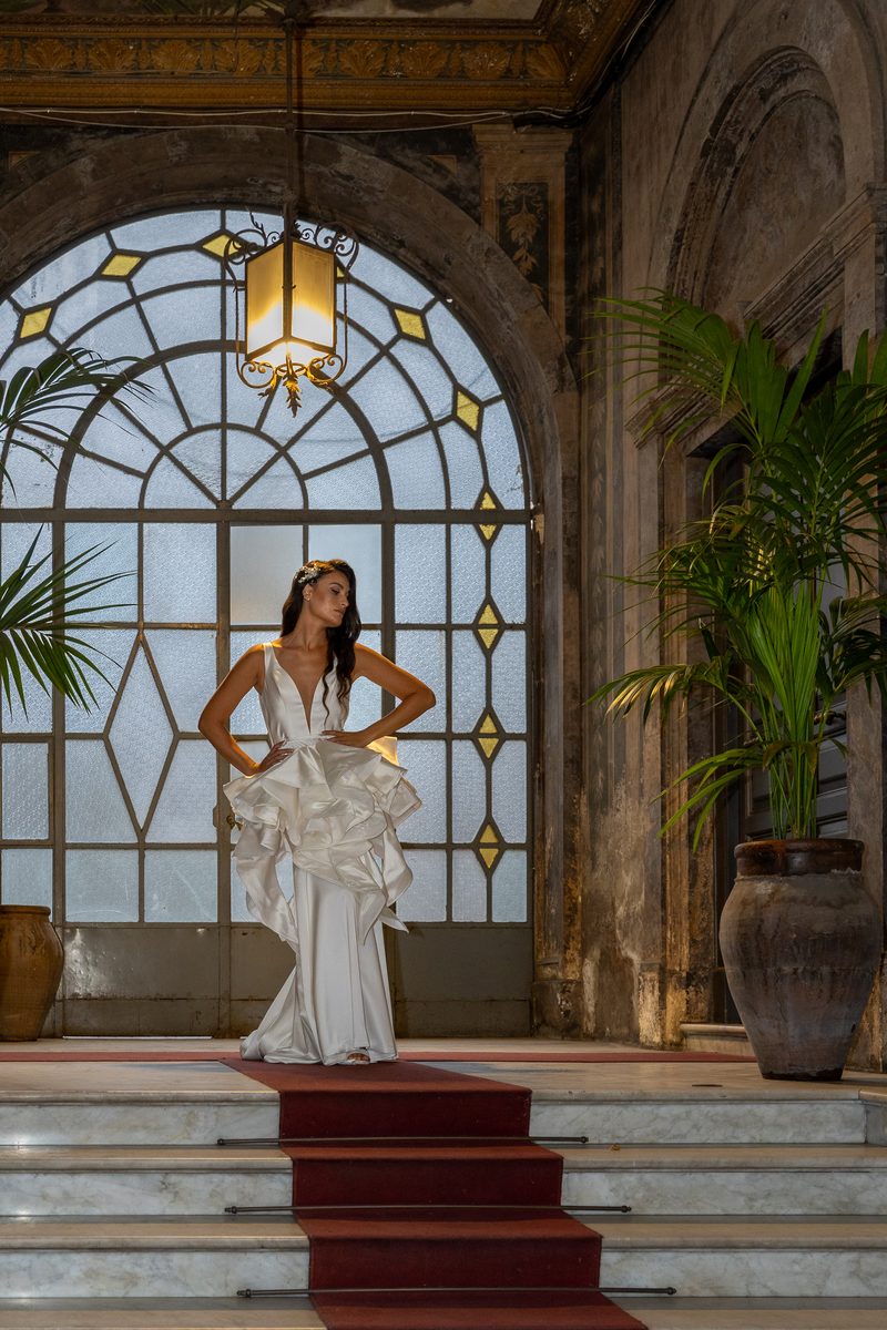 Trunk Show Nagae Bridal: la modella in abito con balze scultoree sotto una vetrata ad arco